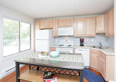 Glenbrook Centre Apartments. Cedar Rapids Iowa. Kitchen. Window with blinds. Wood cabinets. Refrigerator. Electric stove top and oven. Microwave. Dual stainless steel sink. Dishwasher. Wood flooring. Large table in kitchen. Tile backsplash.
